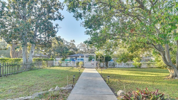 A pathway leading to a house with a white fence and trees on either side.