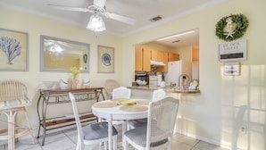 A dining area with a round table, white chairs, and a ceiling fan.