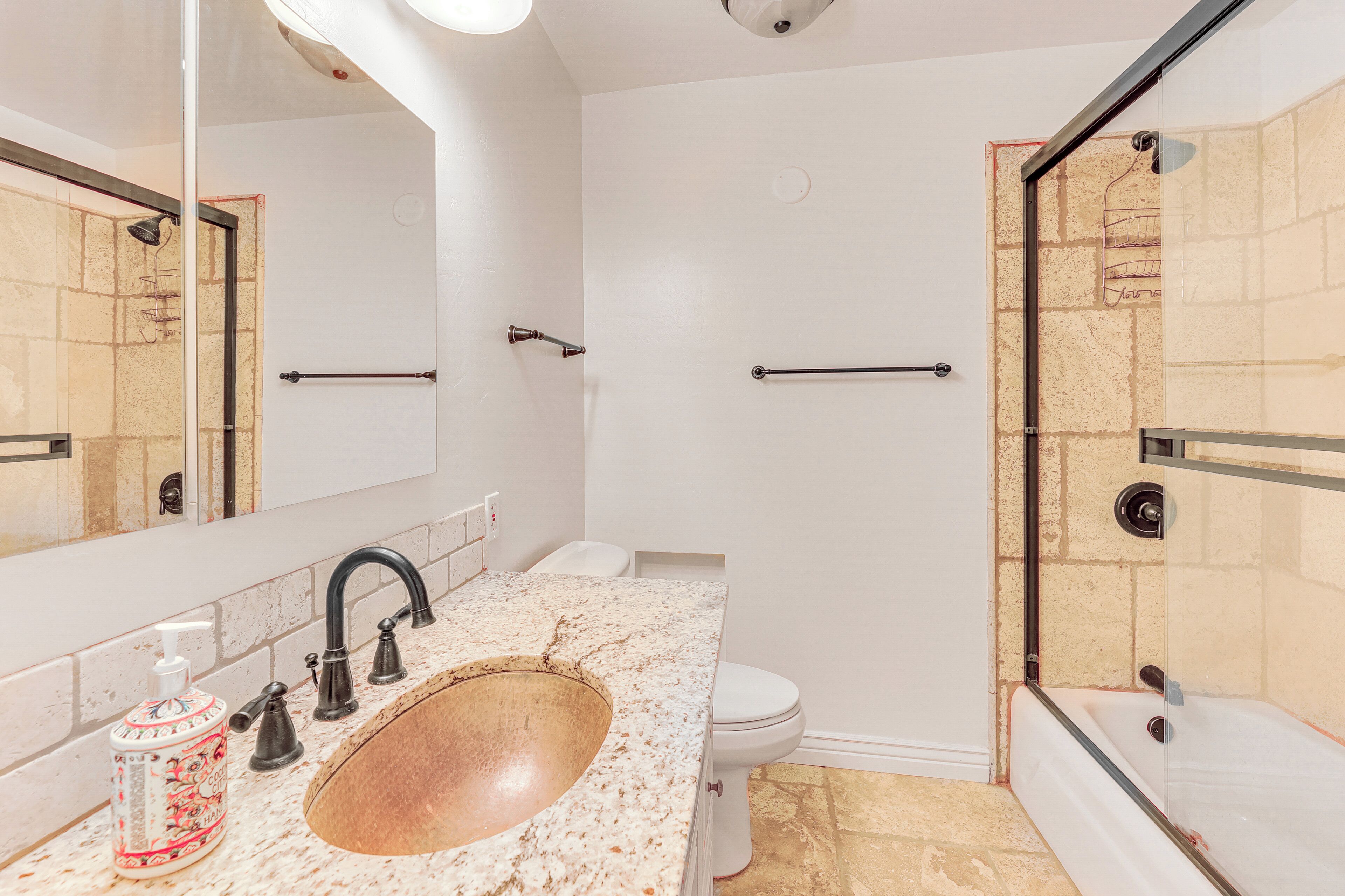 A bathroom with a marble sink, a large mirror, a shower with a glass door, and a toilet.