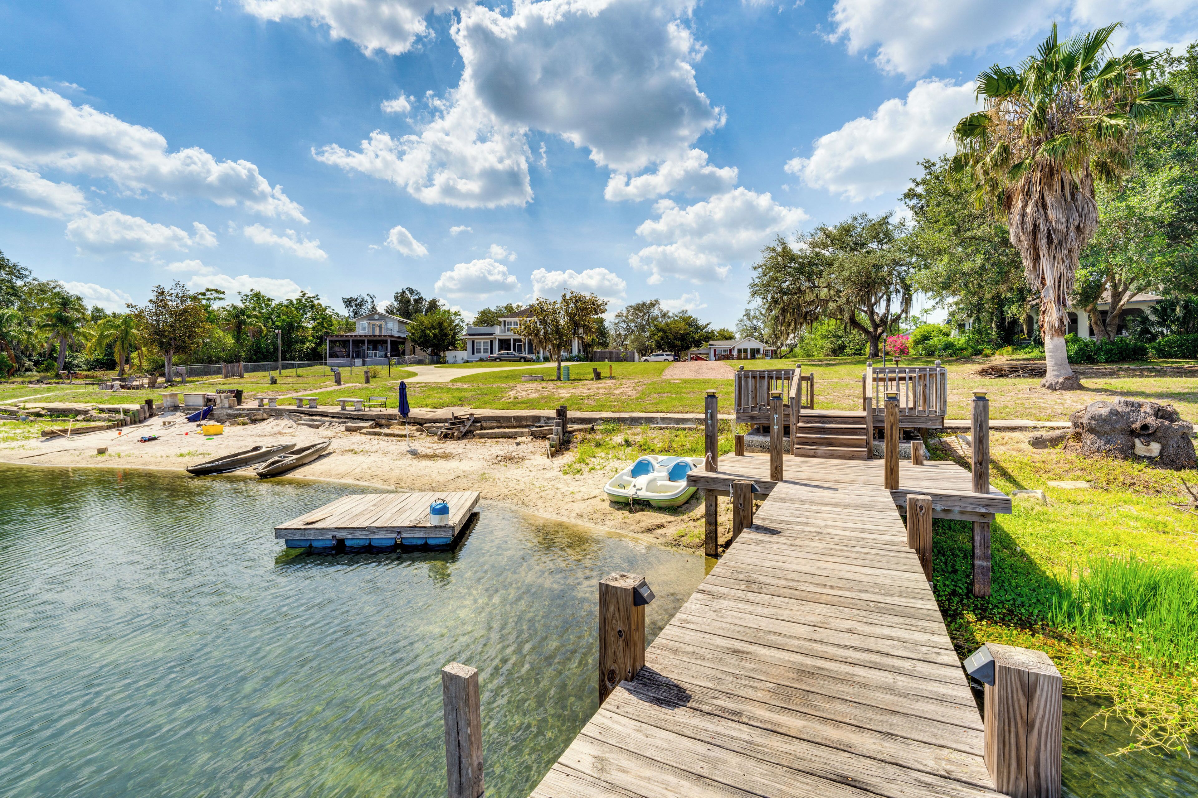 A wooden dock extending into a calm body of water, surrounded by greenery and a clear sky.