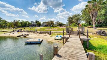 A wooden dock extending into a calm body of water, surrounded by greenery and a clear sky.