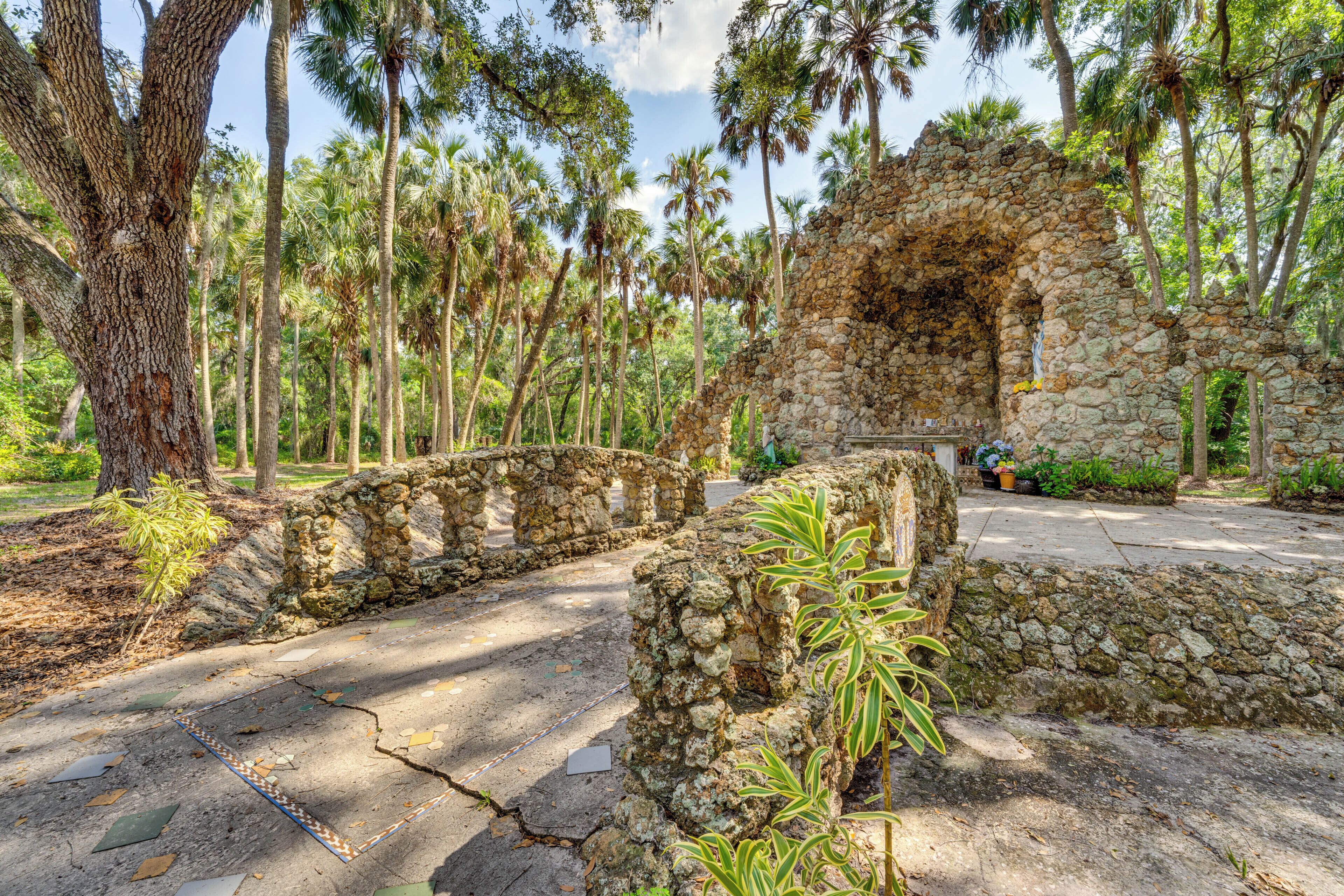 A stone archway leading to a stone building surrounded by tall palm trees.