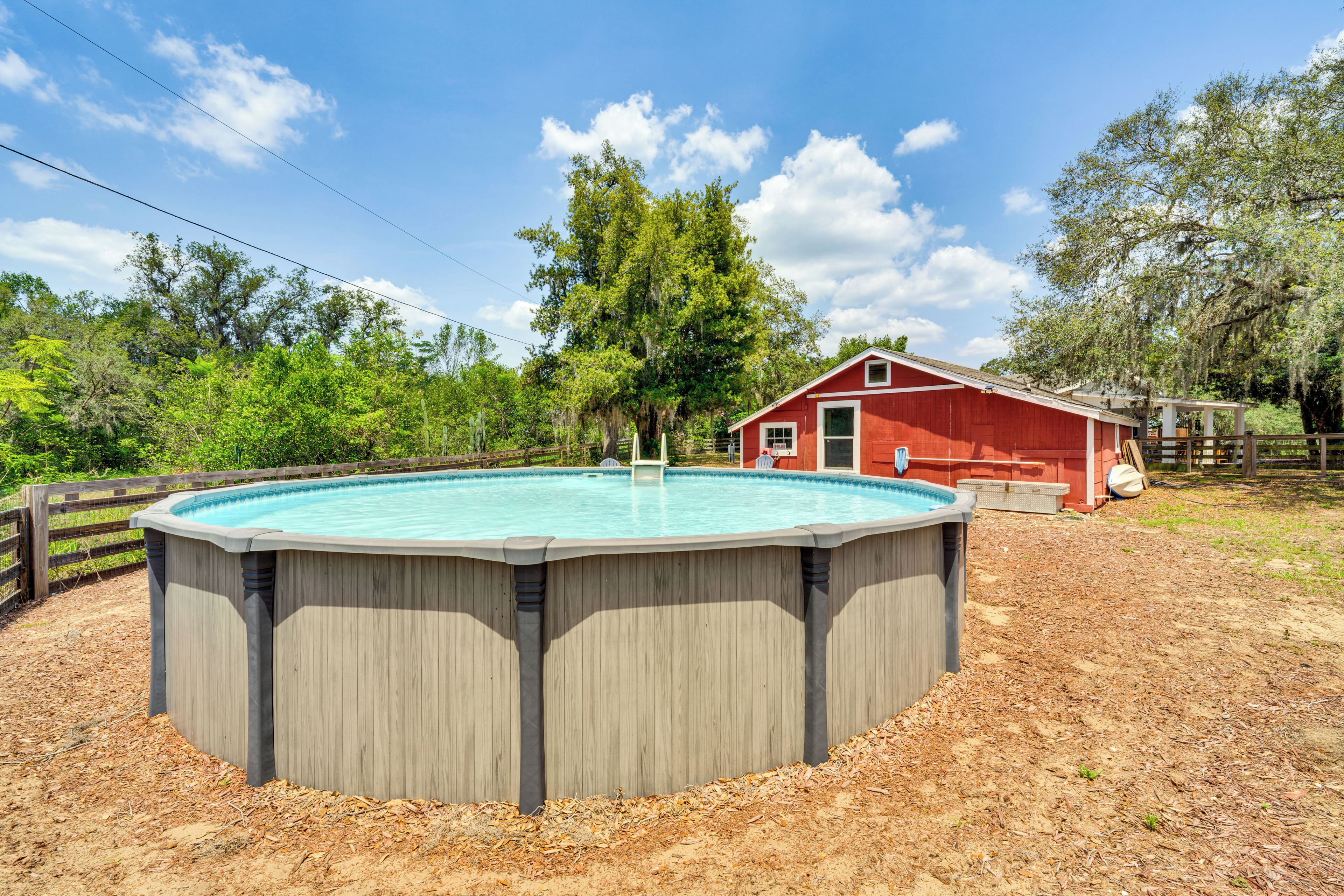 A circular pool with a wooden deck, surrounded by a wooden fence, with a red barn in the background.