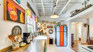 A kitchen with wooden countertops, a coffee machine, and various kitchen utensils. There are framed pictures on the wall and a window with curtains. - Artsy Bungalow on St Anne Lake: Pool, Dock & Deck (Lake Wales)