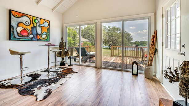 A spacious room with a large sliding glass door leading to a deck, a ceiling fan, a cowhide rug, and a colorful abstract painting. - Artsy Bungalow on St Anne Lake: Pool, Dock & Deck (Lake Wales)