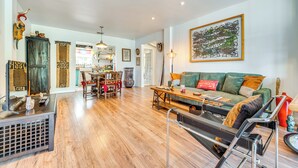 A spacious living area with a wooden floor, a green sofa with orange cushions, a black sofa, a dining table with chairs, and a kitchen in the background. - Artsy Bungalow on St Anne Lake: Pool, Dock & Deck (Lake Wales)