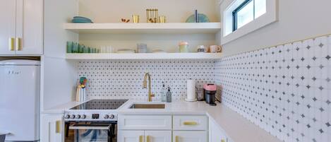A compact kitchen with white cabinetry, a built-in oven, a sink, and a window above the countertop.