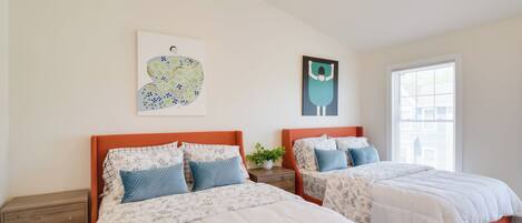Een slaapkamer met twee bedden, een nachtkastje, een plafondventilator en kunstwerken aan de muur.