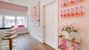A hallway with a row of gold bar stools, a white door, and a wall with pink wine glasses and a pink flower arrangement. - 2 Mi to TBK Bank Sports Complex: Townhome w/ Patio (Bettendorf)