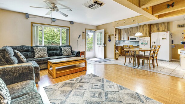 Ein geräumiges Wohnzimmer mit einer Couch, einem Couchtisch und einem gemusterten Teppich. Ein Essbereich mit Tisch und Stühlen ist ebenfalls zu sehen. Der Küchenbereich ist mit modernen Geräten und Holzschränken ausgestattet.