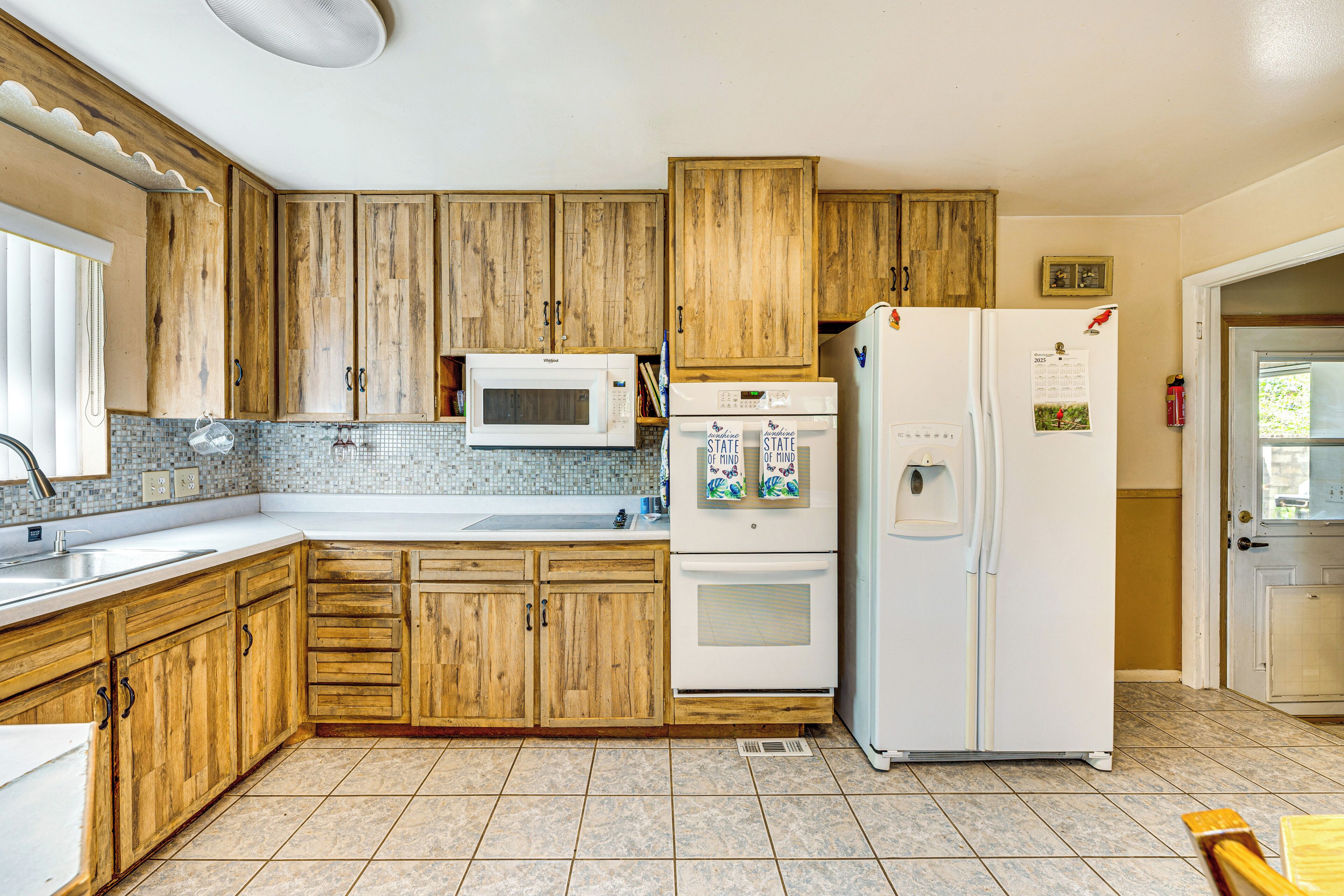 A kitchen with wooden cabinets, a microwave, a refrigerator, and a tiled backsplash.