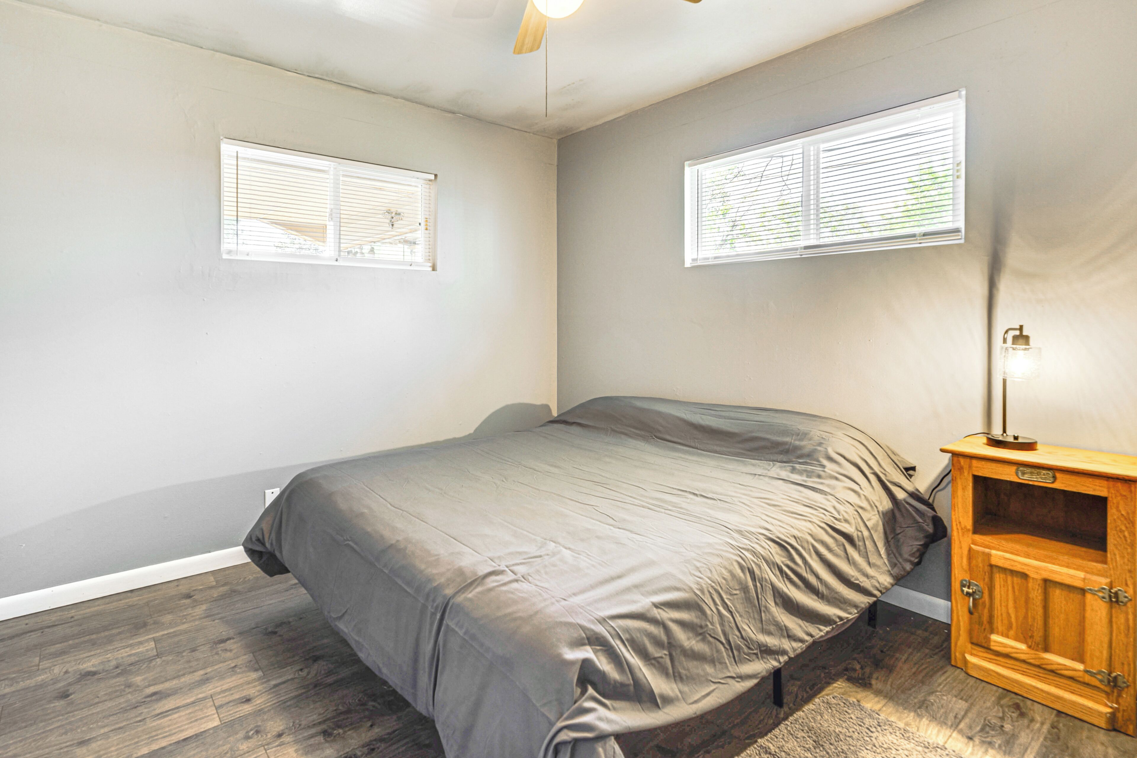 A bedroom with a bed, two windows, a wooden cabinet, and a ceiling fan.