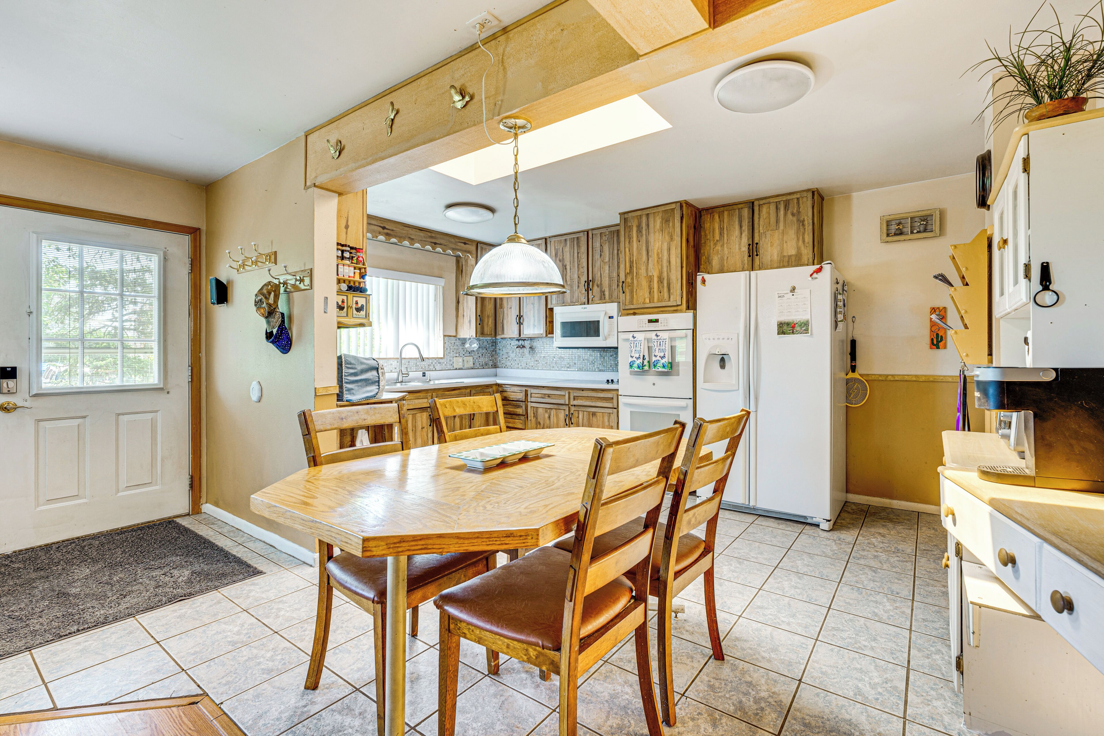 Una cocina con armarios de madera, una mesa de comedor con sillas, un microondas y un refrigerador.
