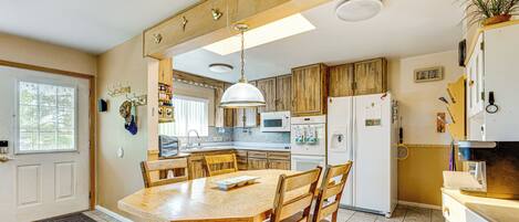 A kitchen with wooden cabinets, a dining table with chairs, a microwave, and a refrigerator.
