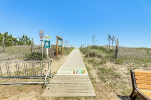 A wooden boardwalk leading to a beach, with a sign indicating public access and a wooden bench on the right.