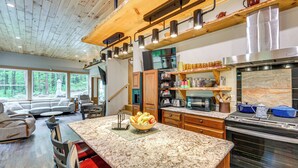 A modern kitchen with granite countertops, a built-in oven, and a large window overlooking a forest.