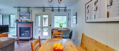 A dining area with a wooden table, chairs, a bowl of fruit, a fireplace, and a television.