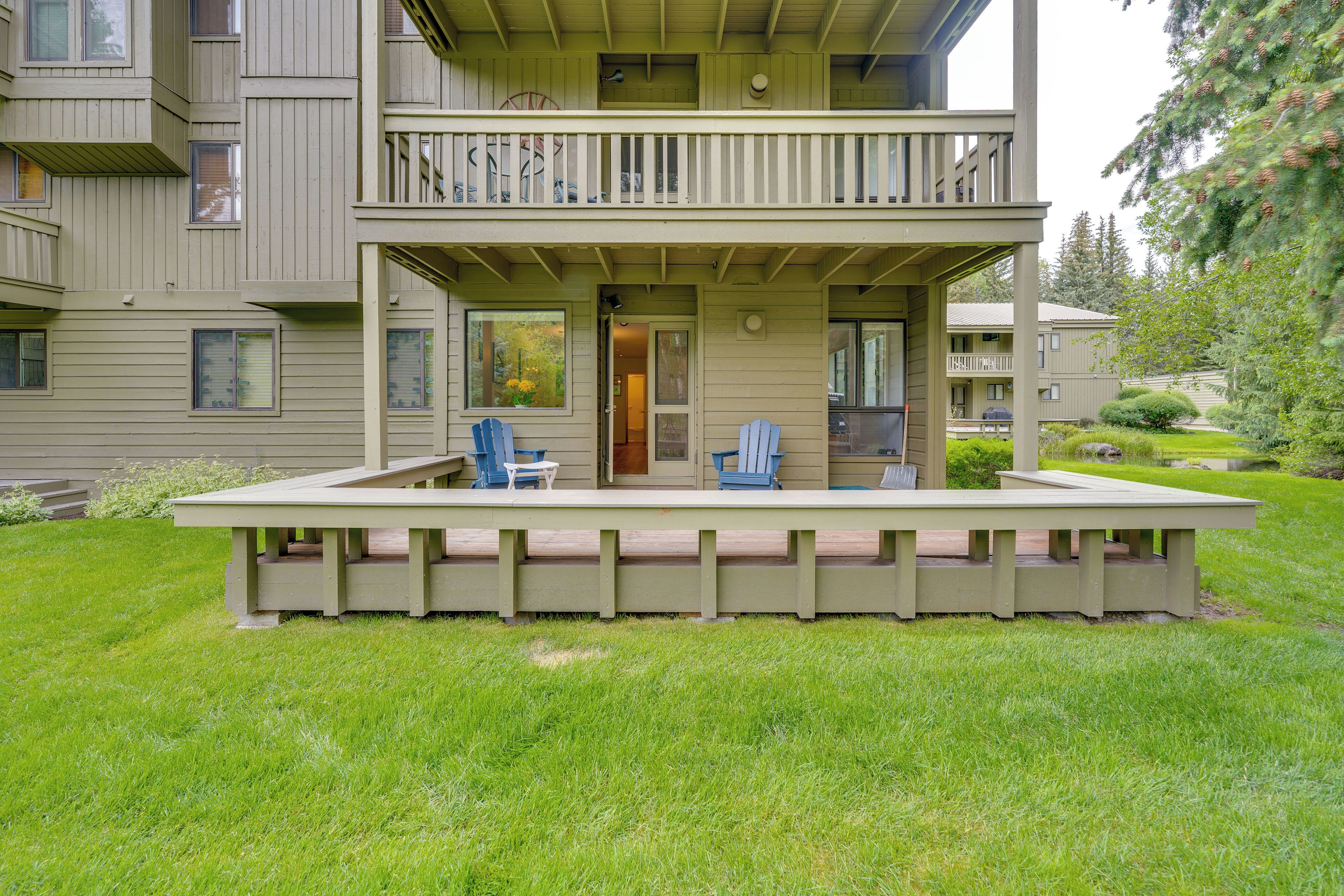Een gebouw met twee verdiepingen, een balkon en een overdekt terras met stoelen, en een verzorgd gazon.