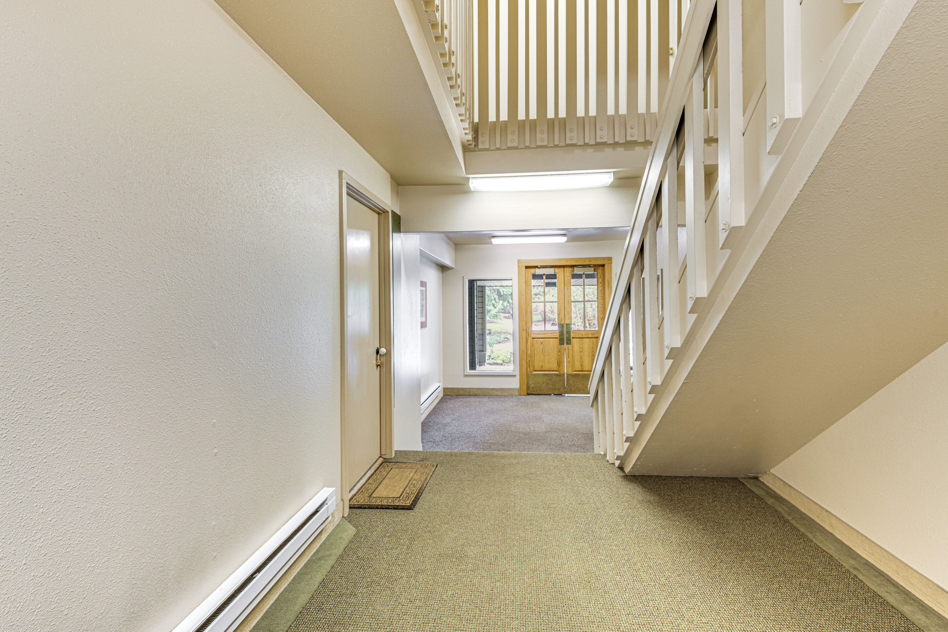 A hallway with a carpeted floor, a wooden door, and a staircase with white railings.