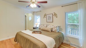Un dormitorio con cama, ventilador de techo, ventana con vistas y un cuadro en la pared.