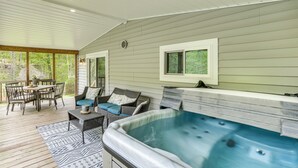 Un espacio al aire libre techado con un jacuzzi, mobiliario de mimbre y una mesa de comedor.