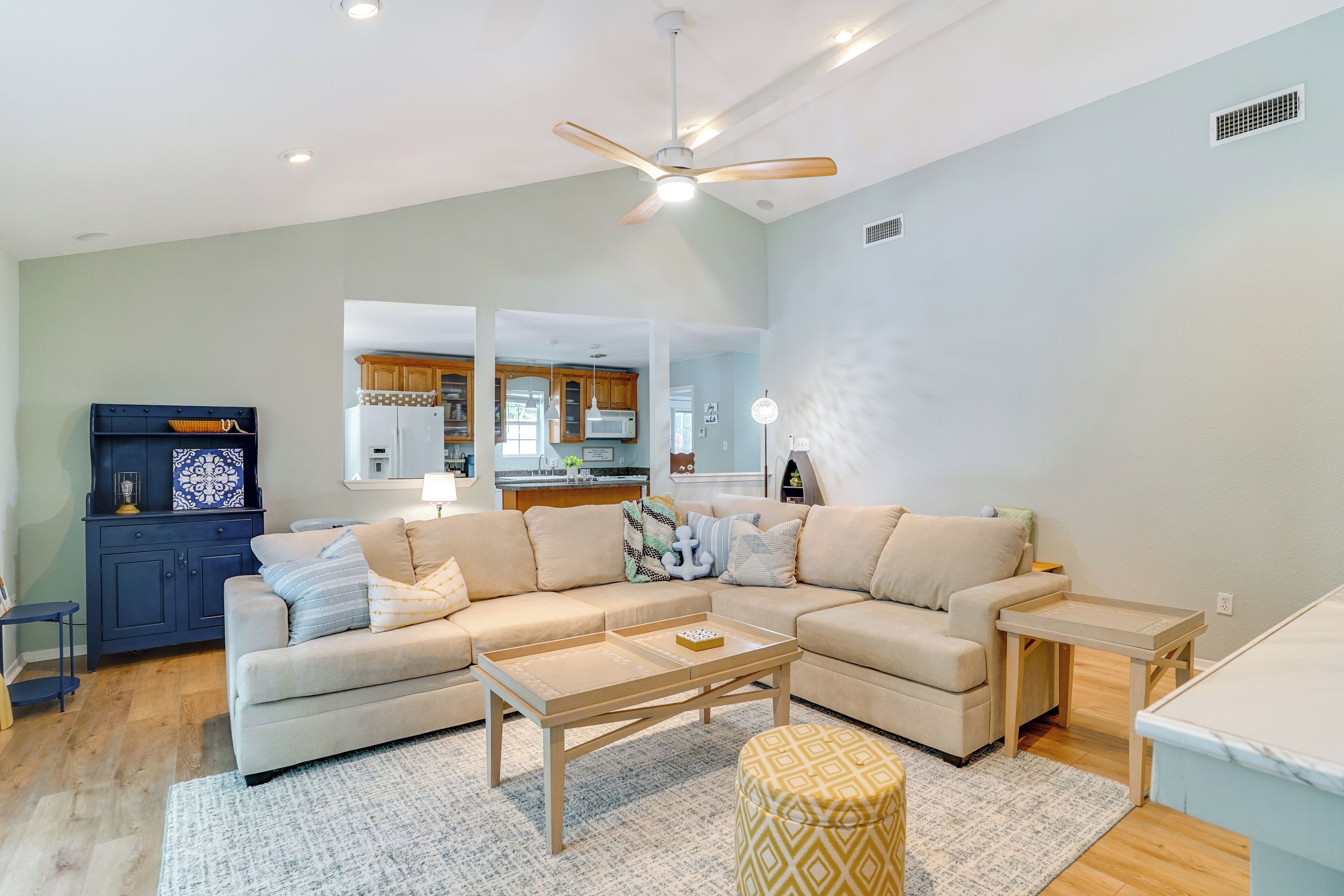 A spacious living room with a beige sectional sofa, a wooden coffee table, and a ceiling fan.
