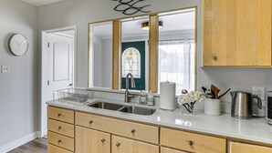 A kitchen with a double sink, wooden cabinets, a stainless steel kettle, and a clock on the wall. - 4 Boat Slips: Getaway on Mouth of Clinton River! (Harrison)