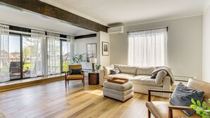 A spacious living room with a large window, a sofa, a chair, and a coffee table. - 4 Boat Slips: Getaway on Mouth of Clinton River! (Harrison)