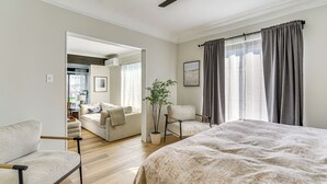A modern bedroom with a large bed, a sitting area with a sofa, and a chair. There is a potted plant and a window with curtains. - 4 Boat Slips: Getaway on Mouth of Clinton River! (Harrison)