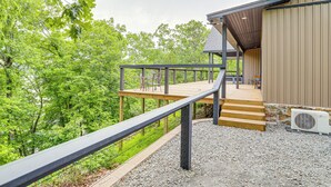 Une terrasse en bois avec une rambarde en métal, menant à un bâtiment doté d’un toit en pente et de fondations en pierre.