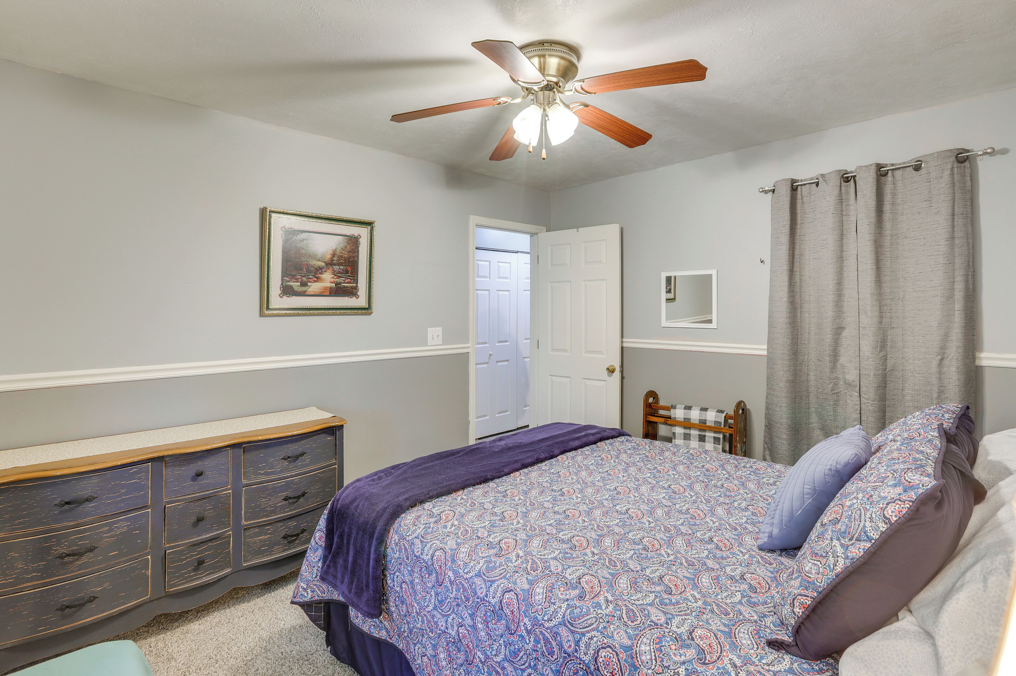 A bedroom with a bed, dresser, ceiling fan, and a door.