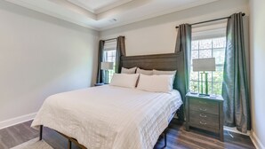 Ein Schlafzimmer mit einem großen Bett, einem Nachttisch, einer Kommode und einem Fenster mit Vorhängen.