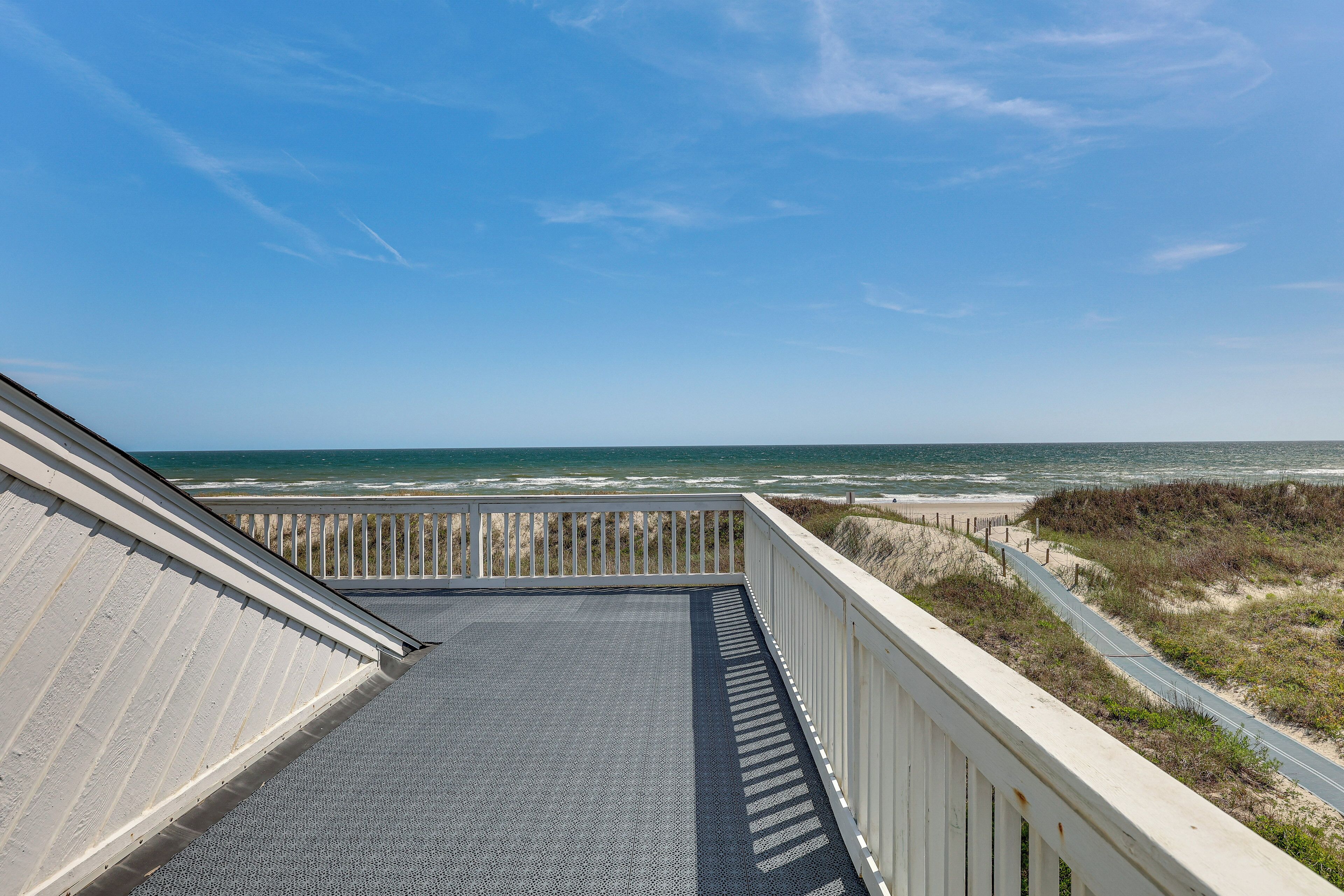 A beach view from a balcony with a paved floor, wooden railing, and a clear sky.