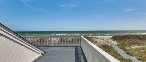A beach view from a balcony with a paved floor, wooden railing, and a clear sky.