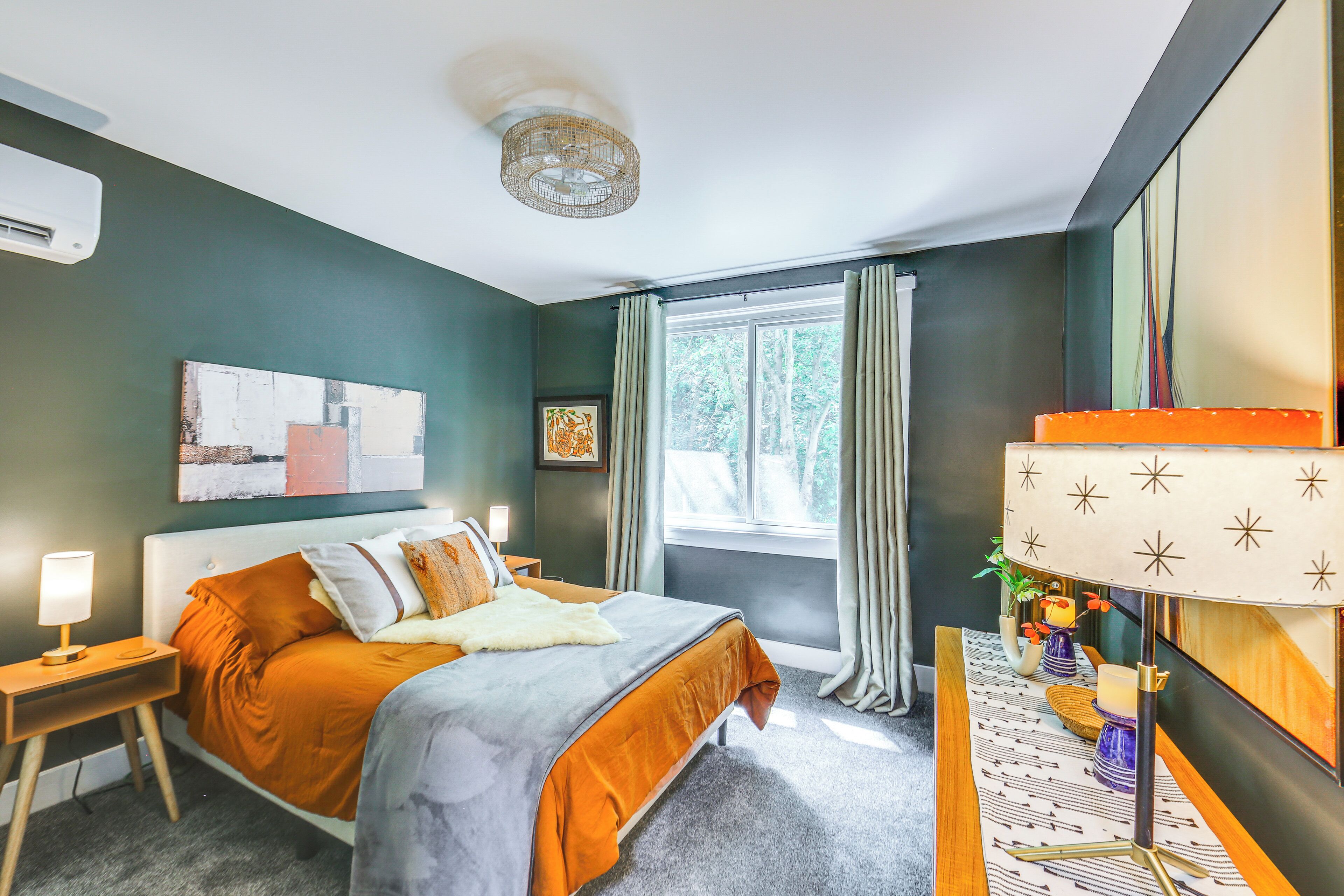 A modern bedroom with a large bed, a bedside table, a lamp, and a view of the outdoors through a window.
