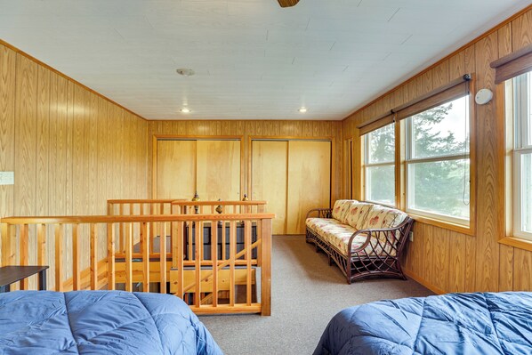 A room with wooden walls, a bunk bed, a wooden crib, a sofa, and a large window. - Walk to Wyalusing Beach: Cabin w/ River View! (Bagley)