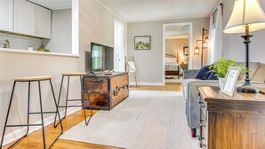 Una sala de estar moderna con un sofá, una mesa de centro y un televisor. Se observa una zona de cocina con armarios y una encimera.