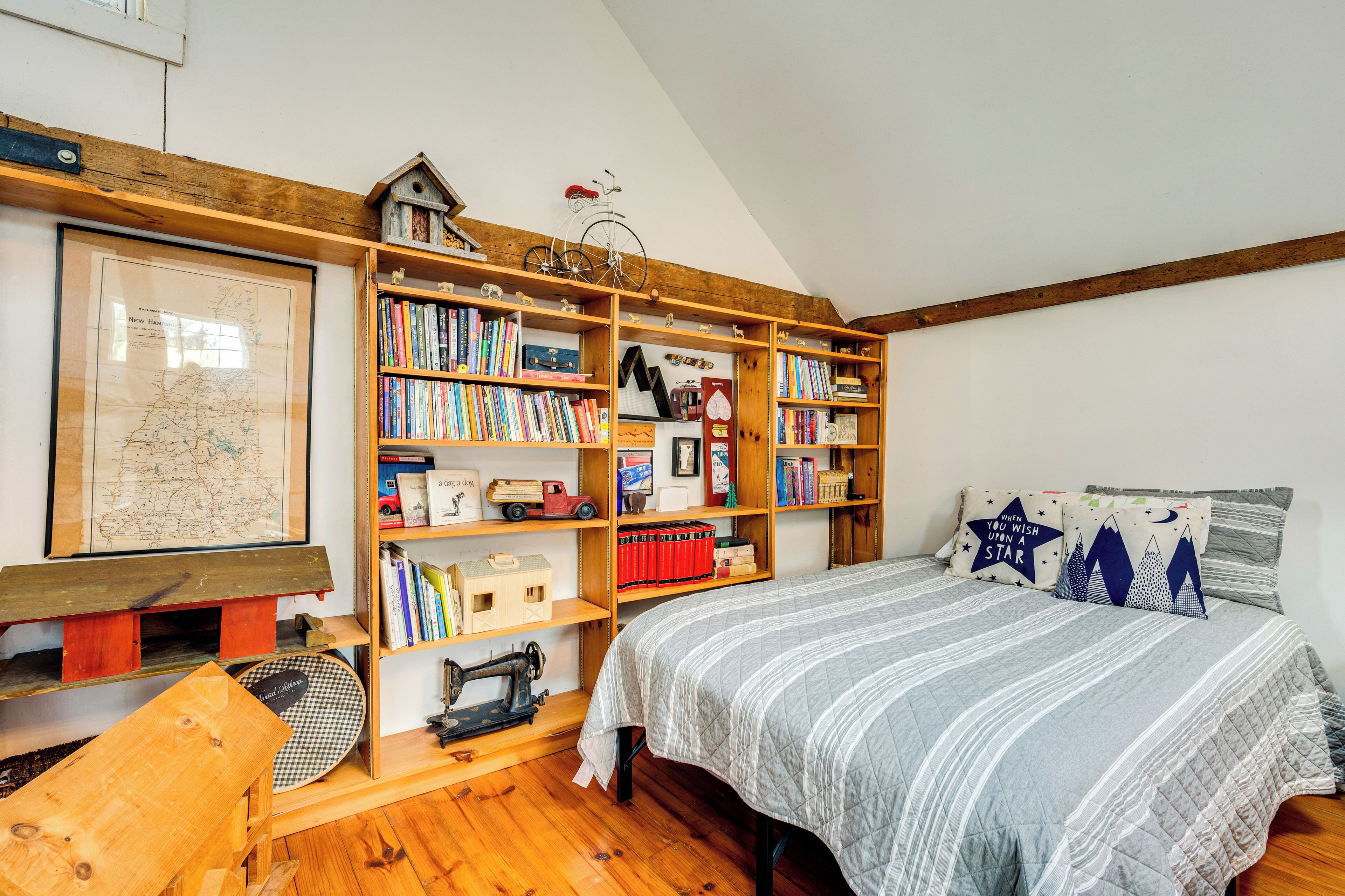 Een knus slaapkamer met een houten boekenkast, een kaart, een naaimachine en een bed met gestreept beddengoed.