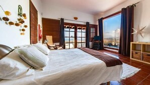 A bedroom with a bed, a chair, a desk, and a view of the city. - Villa Vista Mar (Tias)
