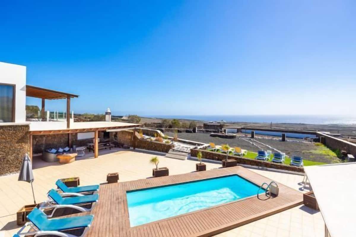 A rooftop pool with lounge chairs, a pergola, and a view of the coastline.