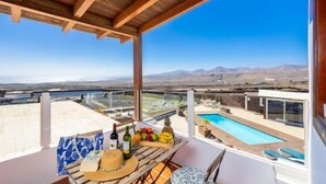 A balcony with a wooden ceiling, a table with fruits and bottles, and a pool view. - Villa Vista Mar (Tias)