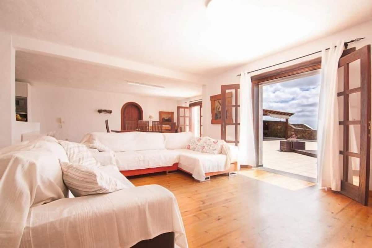 Una habitación con piso de madera, un sofá blanco, una puerta de madera y vistas a un balcón.