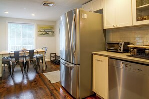 Una cocina moderna con electrodomésticos de acero inoxidable, un comedor con mesa y sillas, y un ventanal con persianas.