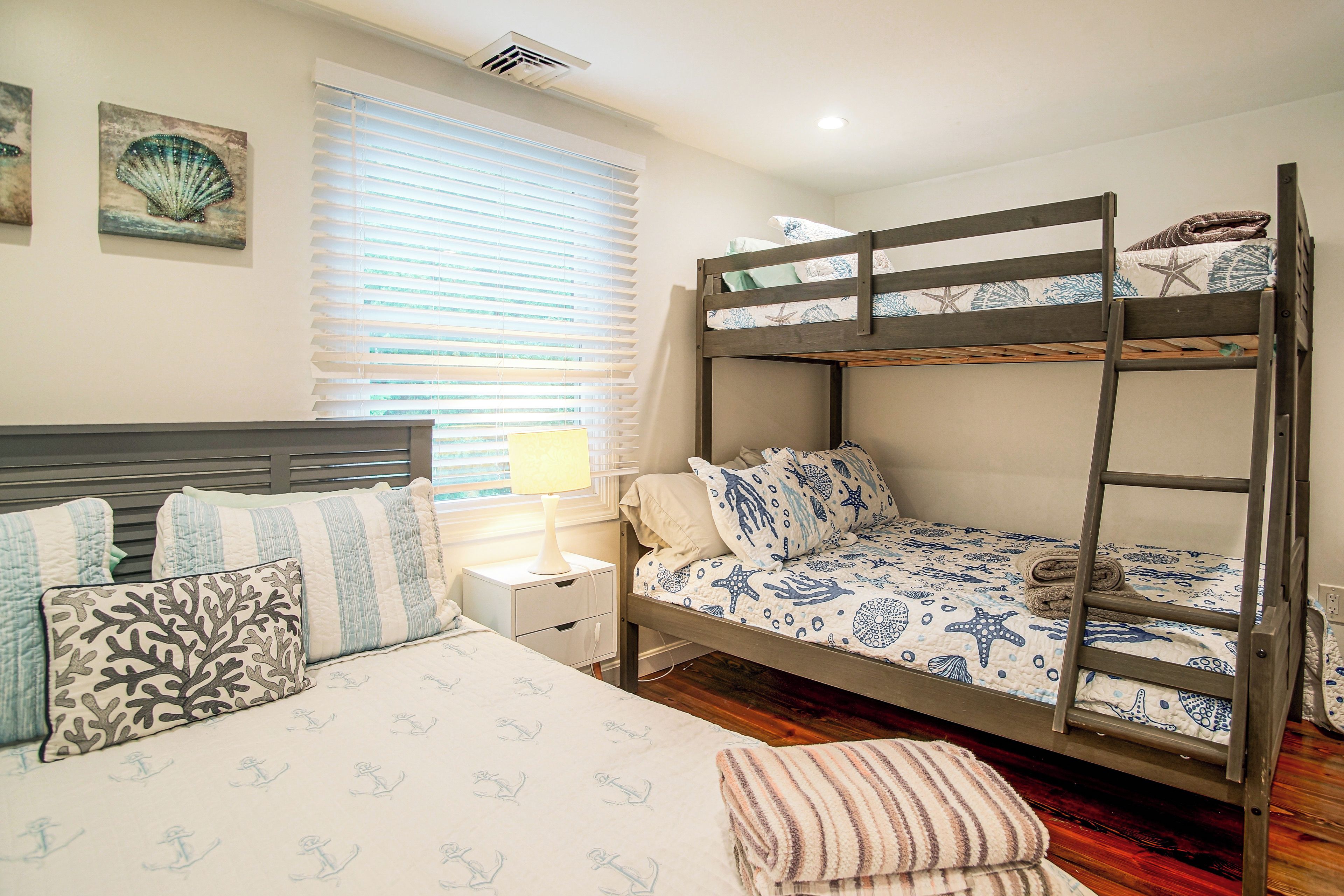 A bunk bed with a nautical theme, a bedside table with a lamp, and a window with blinds.