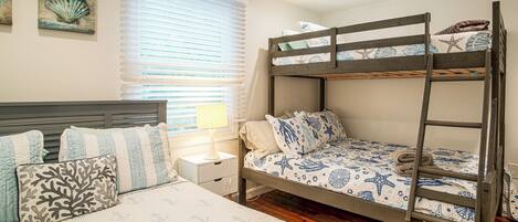 A bunk bed with a nautical theme, a bedside table with a lamp, and a window with blinds.