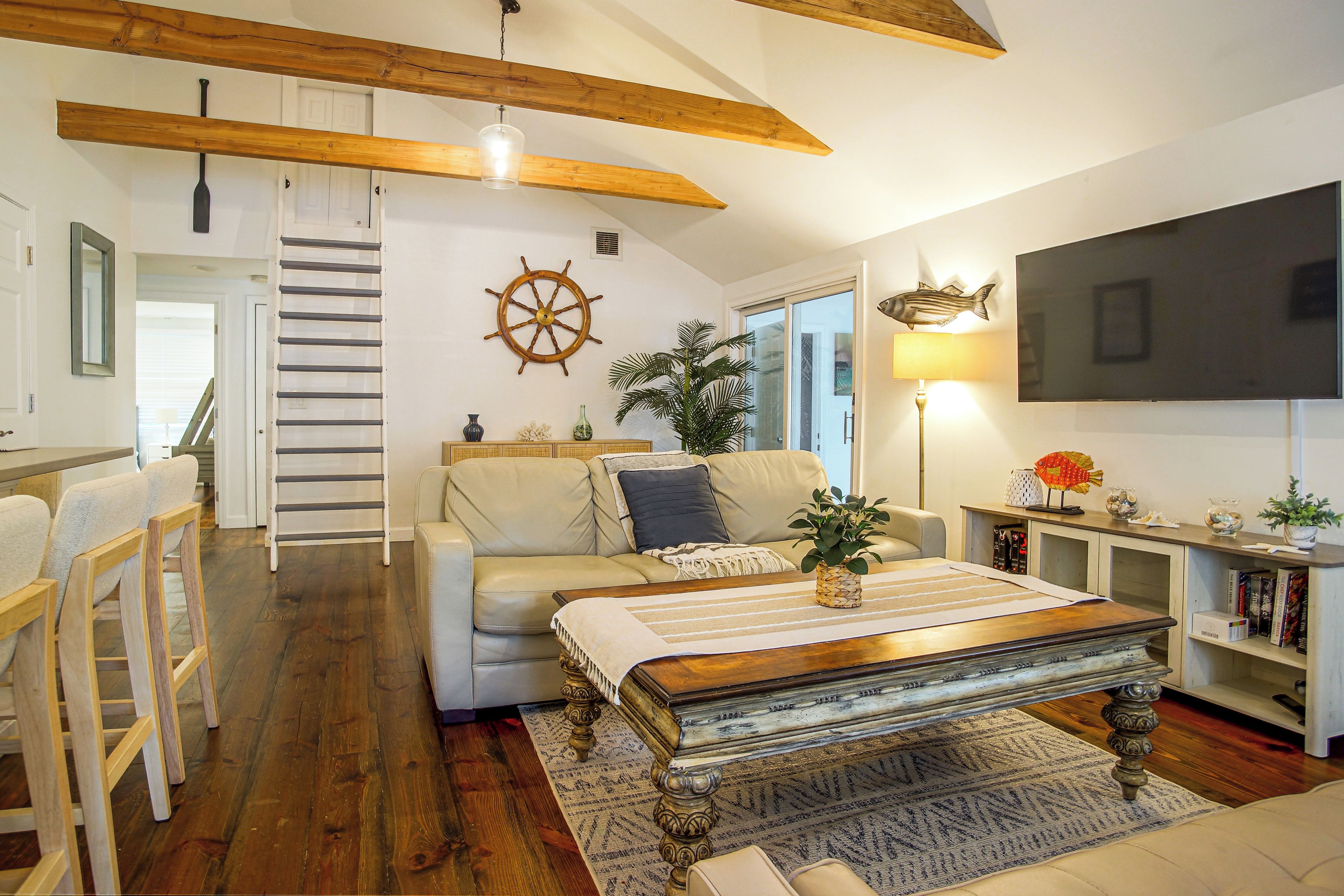 Uma sala de estar acolhedora com piso de madeira, um sofá, uma mesa de centro e uma TV na parede.
