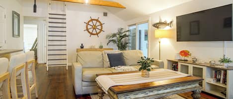 Een gezellige woonkamer met houten vloer, een bank, een salontafel en een aan de muur bevestigde televisie.