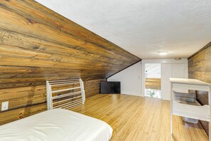Un dormitorio con paredes de madera, una cama, un radiador blanco, un televisor y un escritorio.