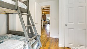 Uma cama beliche com escada, uma porta branca e um piso de madeira.