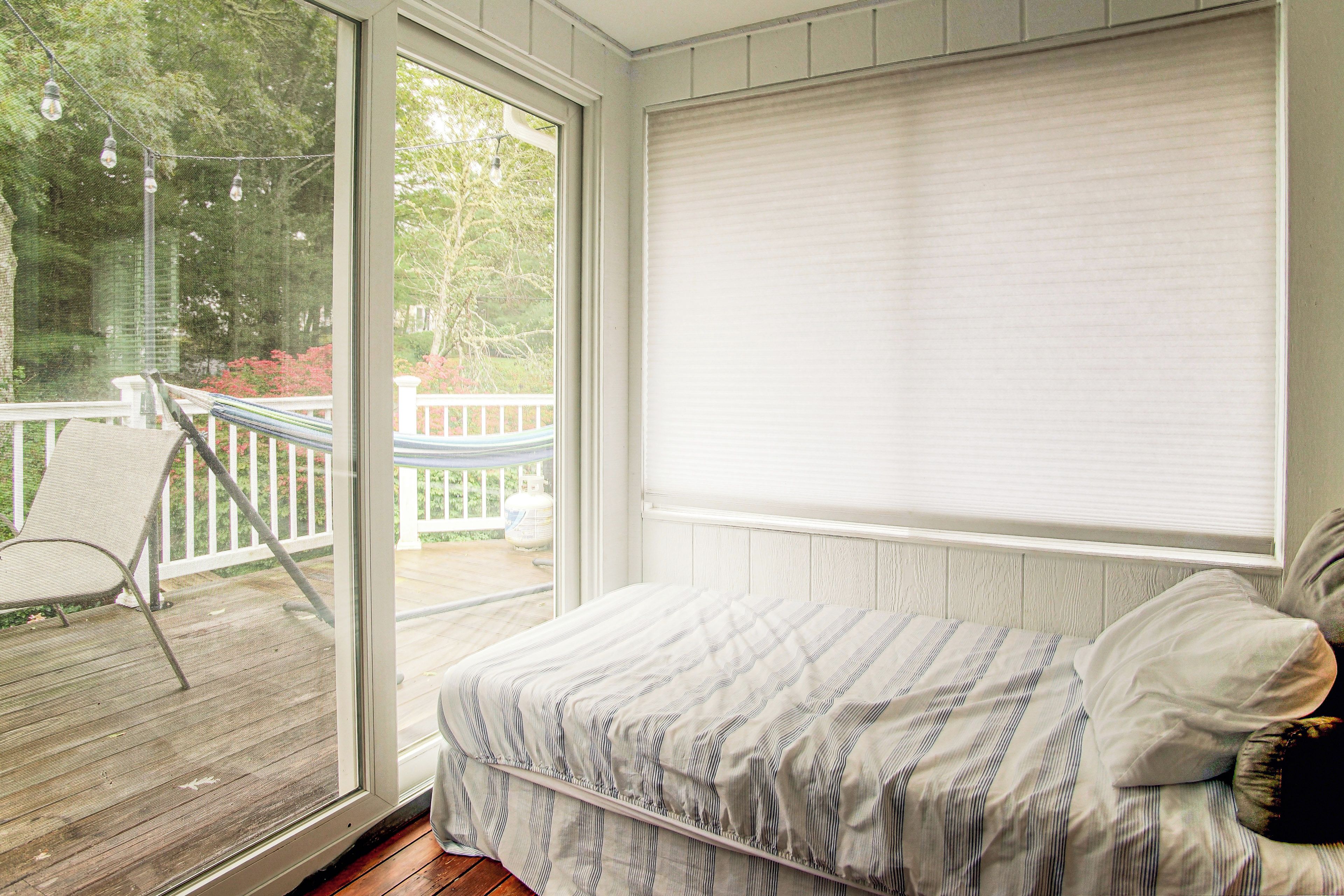 Quarto com cama, janela com persianas, vista para um deck e uma cadeira.